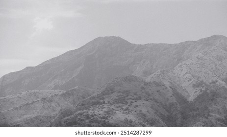 A mountain range with a cloudy sky in the background. The mountains are covered in trees and the sky is overcast