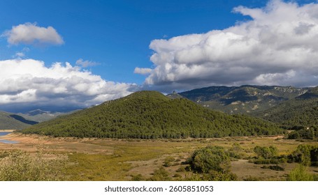 A mountain range with a cloudy sky in the background. The sky is blue and the clouds are white