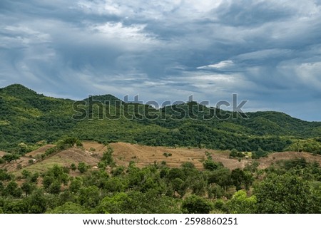 A mountain range with a cloudy sky in the background. The sky is overcast and the mountains are covered in trees