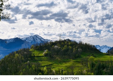 Mountain range with a cloudy sky and a small house in the middle. The house is surrounded by trees and the mountains are covered in snow. The scene is peaceful and serene