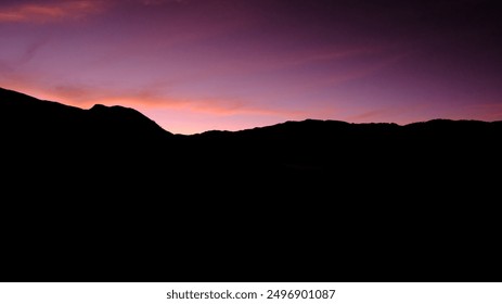 A mountain range with a dark sky and a bright orange sun. The sun is setting and the sky is a deep purple
