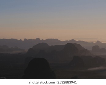 A mountain range with a hazy sky in the background. The mountains are covered in a misty haze, giving the scene a serene and peaceful atmosphere. The sky is a mix of blue and purple - Powered by Shutterstock