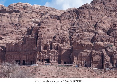 A mountain range with a large building in the middle. The building is surrounded by smaller buildings. The mountain range is rocky and the sky is cloudy
