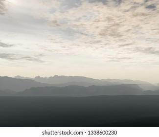 Mountain range in mist under cloudy sky.