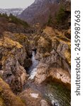 A mountain range with a river running through it. The water is clear and the rocks are grey