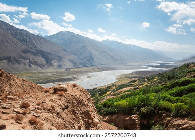 A mountain range with a river running through it. The sky is clear and blue. The mountains are covered in snow and the river is flowing through a valley. The scene is peaceful and serene