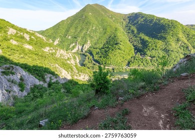 Mountain range with a river running through it. The mountains are lush and green, and the river is calm and peaceful. The scene is serene and picturesque