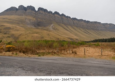 A mountain range with a road in front of it. The road is empty and the sky is cloudy