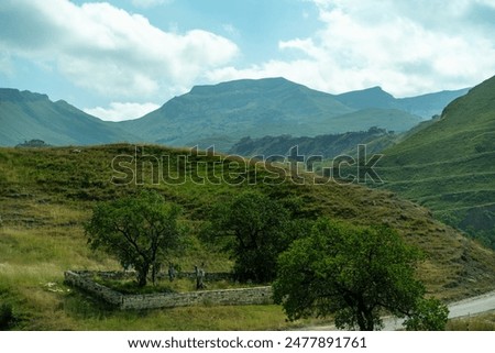 A mountain range with a small house in the middle of the field. The house is surrounded by trees and the mountains are in the background. The scene is peaceful and serene.