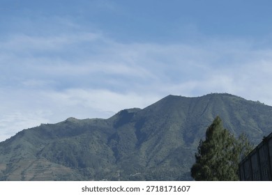 A mountain range with a small town in the valley below. The town is surrounded by green hills and trees