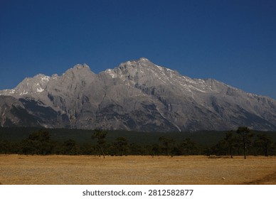 A mountain range with sparse trees in the foreground under a clear blue sky.