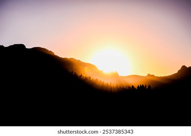 A mountain range with a sun setting behind it. The sun is low in the sky and casting a warm glow over the mountains. The scene is peaceful and serene, with the sun's rays illuminating the landscape