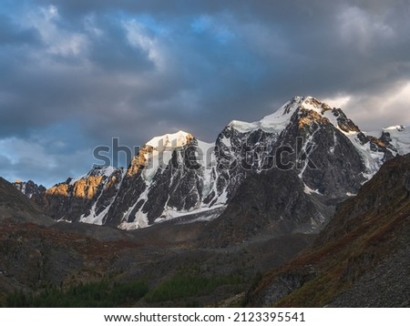 Mountain range at sunrise.Awesome scenery with sunlit snow mountains in cloudy sky at sunrise. Dark scenic landscape with large glacier in sunrise colors.
