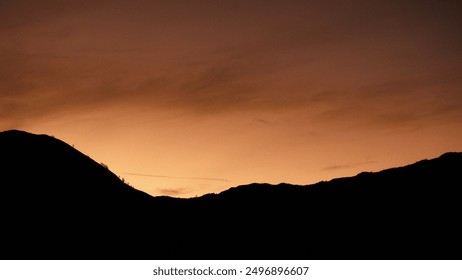 A mountain range with a sunset in the background. The sky is orange and the mountains are silhouetted against the sky