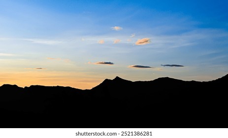 mountain range at sunset, with a clear blue sky and few wispy clouds. the mountains are silhouetted against the colorful sky - Powered by Shutterstock - Get 15% off with code: PIKWIZARD15