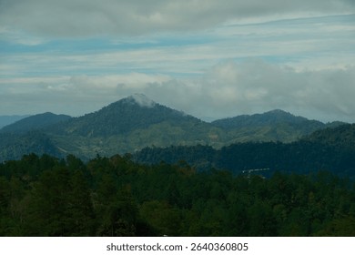 “Layered mountain range under a cloudy sky with blue tones and rolling hills stretching into the distance.”
