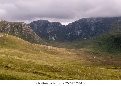 A mountain range with a valley in between. The valley is mostly green and the mountains are mostly gray