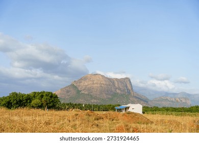 Mountain range is visible in the background with a small house in the foreground. The sky is clear