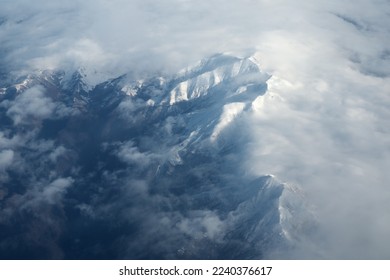Mountain range and white clouds in blue sky at day. View from above air plane.