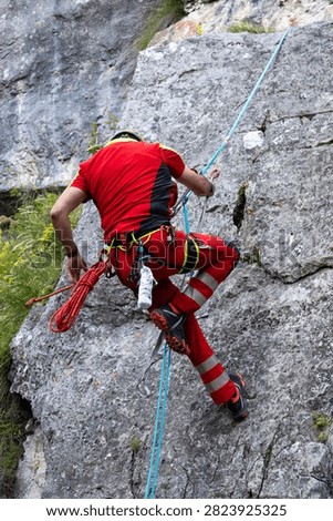 Mountain rescue worker rappelling down a steep rocky cliff during a training session