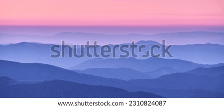 Mountain ridges in fog and pink sky at sunset in autumn. Beautiful landscape with foggy mountain valley, hills, forest at dusk in blue hour in fall. Aerial view of hills. Top view. Nature background