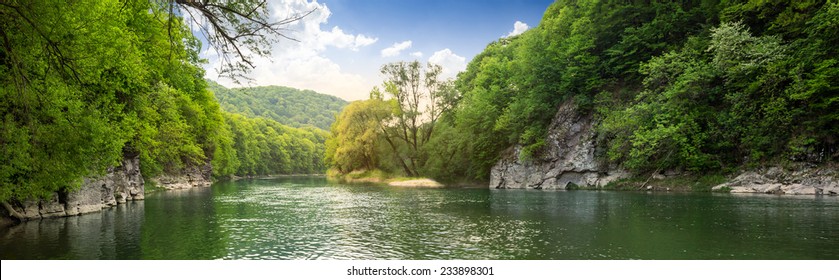 mountain river with stones on the shore in the forest near the mountain slope