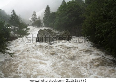 A mountain river or stream raging in a flash flood. Upstream view over the turbulent waters of the upper Gesso river high in the Maritime Alps, Piedmont, Italy, during heavy early summer rains.