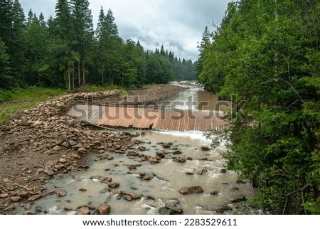 Mountain river. Wooden deck in the river. Shore protection. Carpathians in summer. Mountains of Ukraine.