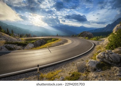 Mountain road at colorful sunset in summer. Dolomites, Italy. Beautiful curved roadway, rocks, stones, blue sky with clouds. Landscape with empty highway through the mountain pass in spring. Travel