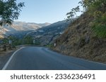 mountain road in La Alpujarra de Granada, there is a town on the mountainside called Capileira, there are trees and bushes, the sky is clear.