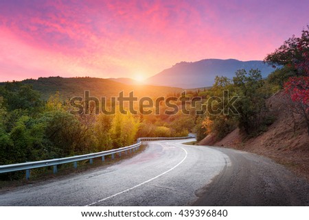 Mountain road passing through the forest with dramatic colorful sky and red clouds at colorful sunset in summer. Mountain landscape with road. travel background