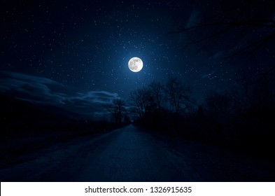 Mountain Road through the forest on a full moon night. Scenic night landscape of country road at night with large moon - Powered by Shutterstock