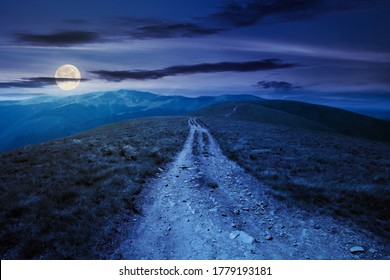 Mountain Road Through Grassy Meadow At Night. Wonderful Summer Adventure In Full Moon Light. Clouds On The Blue Sky