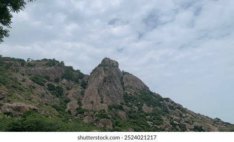 “Majestic Mountain Peak” A rugged hill or mountain rises dramatically against the partly cloudy sky. Its rocky terrain and sparse vegetation evoke a sense of adventure and exploration.
