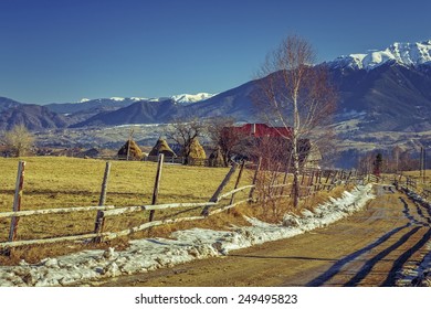 Mountain rural scenery with traditional Romanian farm and muddy country road during winter in the valleys of Bucegi mountains, Brasov county, Romania.