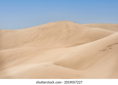 A mountain sand dunes with footmarks against a blue sky