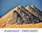 A mountain of sand with three peaks. The sand is white and the sky is blue. Concept of vastness and grandeur