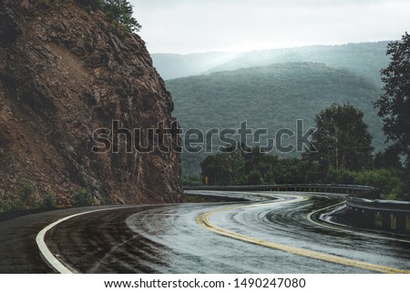 Mountain scenic winding road after rain. Green forest hills in the background covered by fog. Cape Breton, Cabot Trail, Nova Scotia, Canada