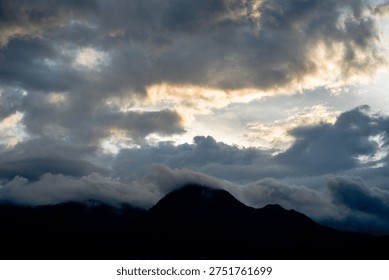 Mountain silhouette under a dramatic cloudy sky during sunset or sunrise