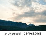Mountain silhouettes under dramatic sunset clouds. Serene dusk landscape with soft light and peaceful tones