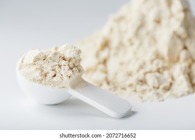 A mountain of soy protein isolate in powder with a measuring spoon on a white background. Vegetarian sports nutrition for cocktails