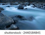 Mountain stream during blue hour with silky water, rapid creek flow around wet rocks in long exposure