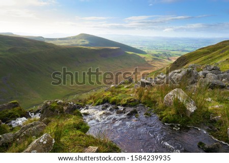 A mountain stream flowing over the edge of High Cup Nick with views of High Cup Gill far below on the Pennine Way.