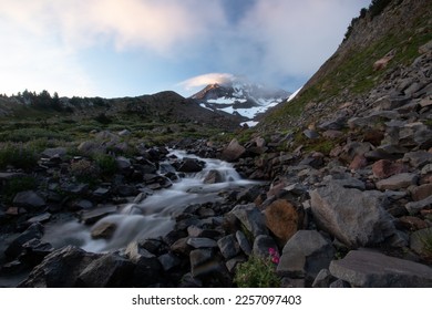 Mountain stream flowing through a rocky meadow with Mt. Hood in swirling clouds. - Shutterstock ID 2257097403
