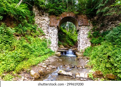 Mountain stream flows through the old stone archway in the forest