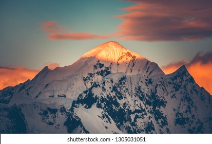 Mountain Top Colorful Sunet, Antarctica. The Sunlit Snow Covered Range. Breathtaking Polar Scenery. The Mighty Mountain Range Under The Bright Sunset Cloudy Sky. Amazing South Pole Landscape.