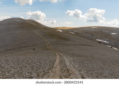 A mountain trail in a treeless mountain range with clouds in a blue sky