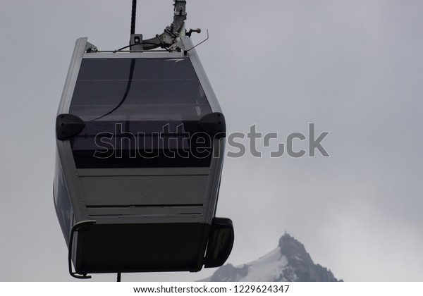 mountain trailer funicular\
gray descends on the background of snow-capped peaks and a mountain\
valley