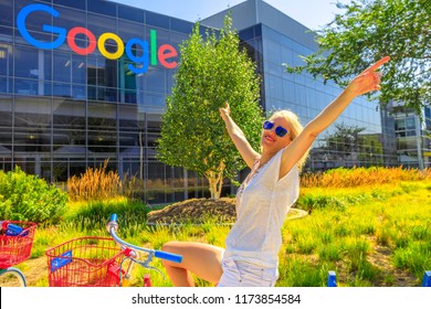 Mountain View, California, USA - August 13, 2018: Smiling Tourist Woman On Google Bike Under Google Sign At Google Headquarters Building. A Young Girl Visiting The Web Leader Company In Silicon Valley