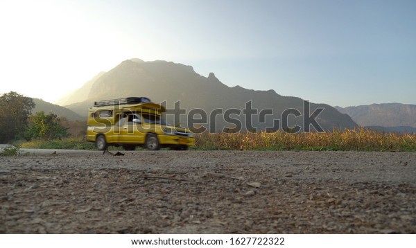 Mountain view\
and yellow car.\
The country road behind is a cornfield and yellow\
car is a passenger car for\
tourists.